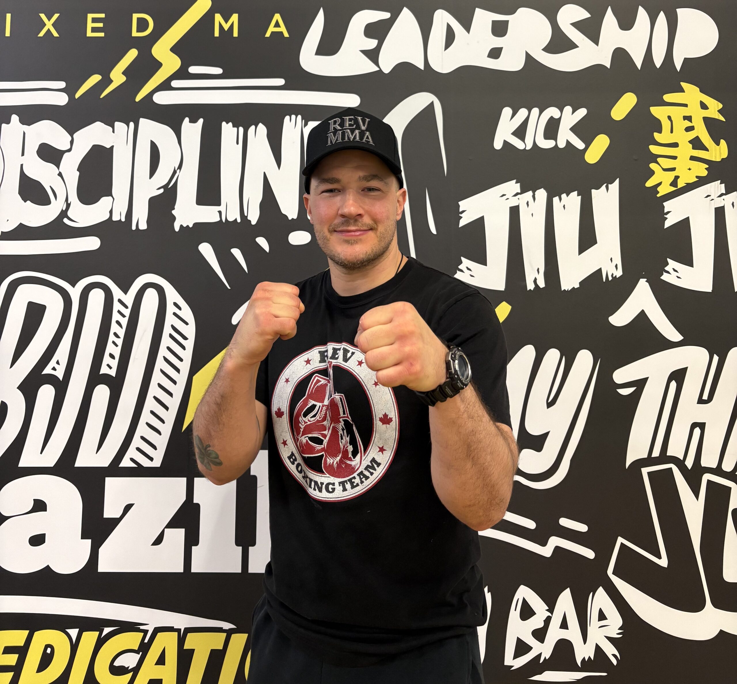 Martial artist posing confidently in front of a motivational wall with Rev Boxing Team shirt and cap.