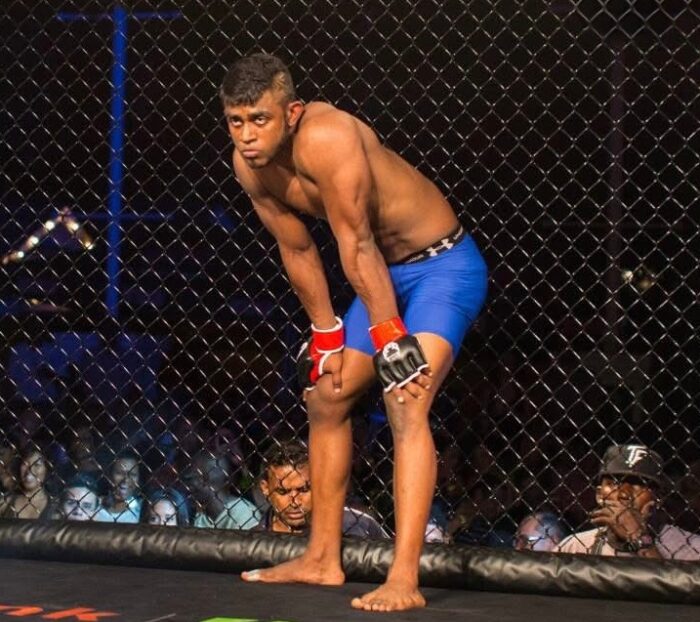 MMA fighter in blue shorts and gloves inside a cage during a match, focused and ready for action.