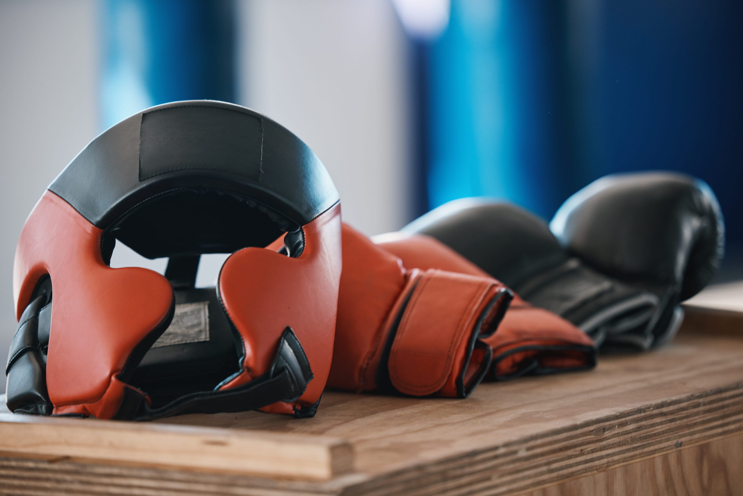Boxing gear on a wooden table, including red protective headgear and gloves in a gym setting.