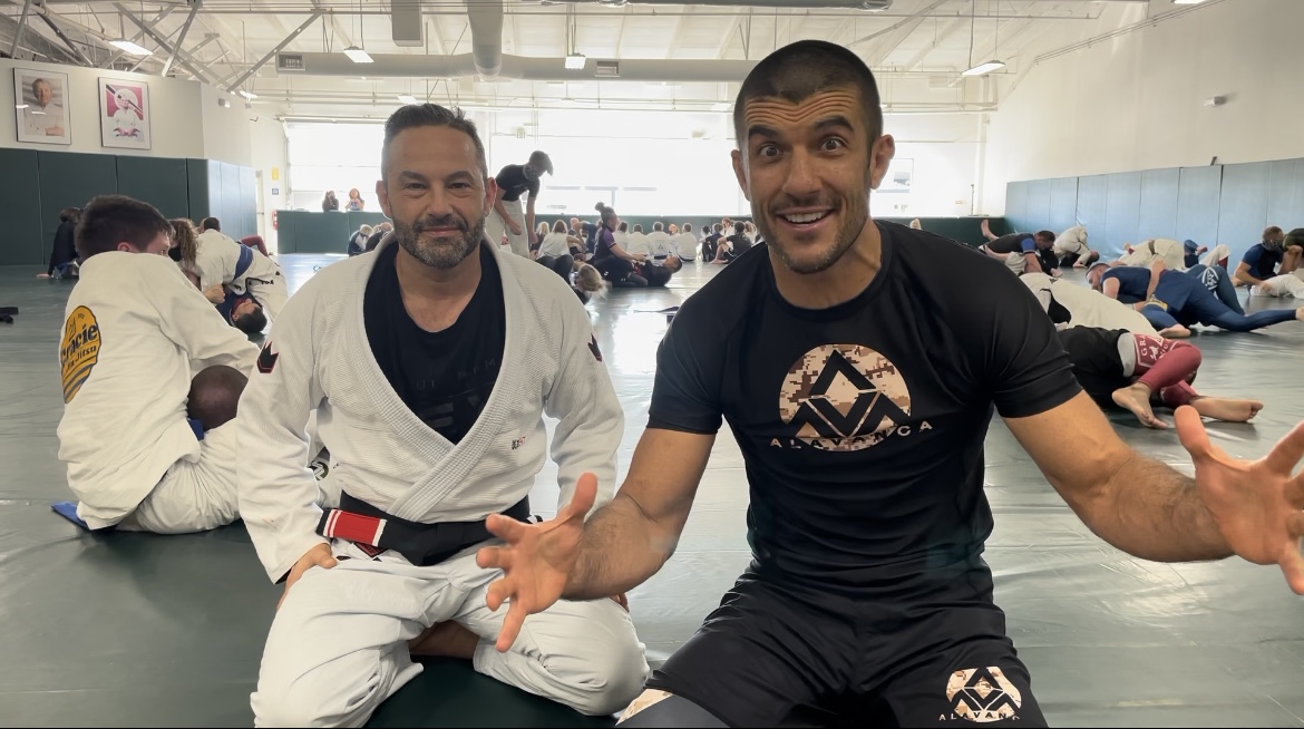 Screenshot Men discussing Brazilian Jiu-Jitsu techniques in a bustling dojo environment.