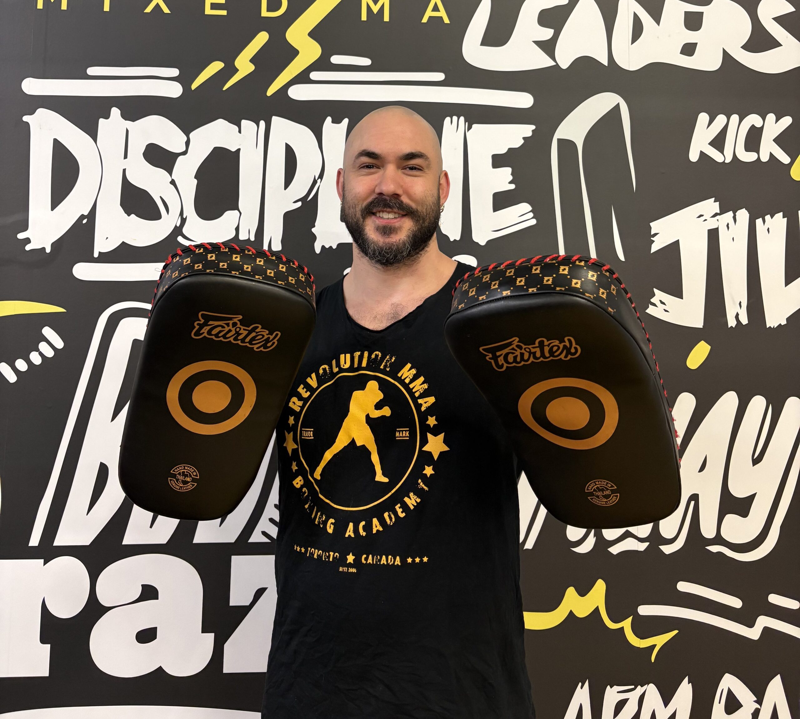 Man holding boxing pads in front of a motivational wall at a martial arts academy.