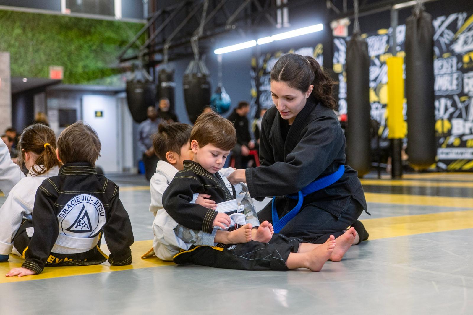 Instructor helps child with jiu-jitsu uniform in martial arts class.
