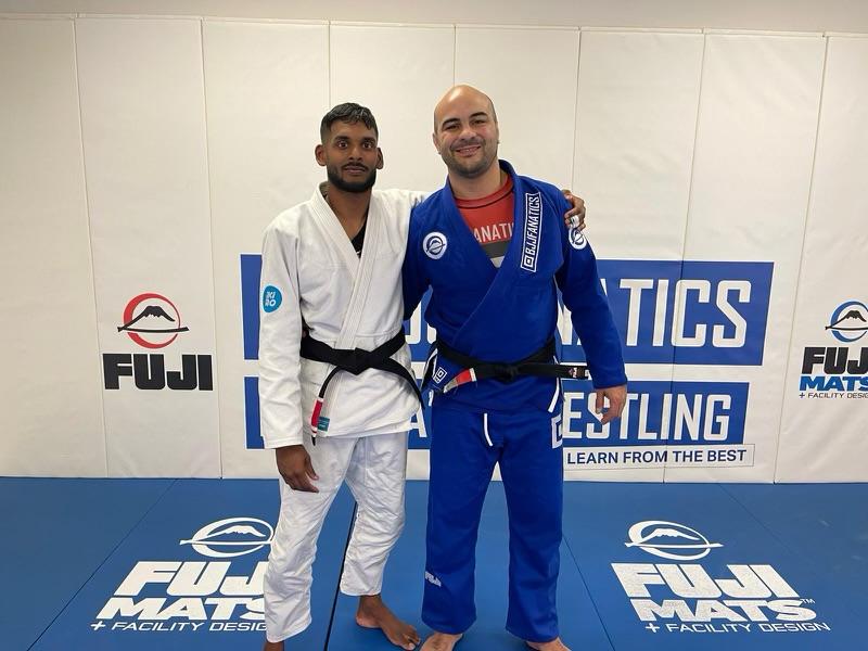 Two men in martial arts uniforms posing on a mat at a jiu-jitsu academy.