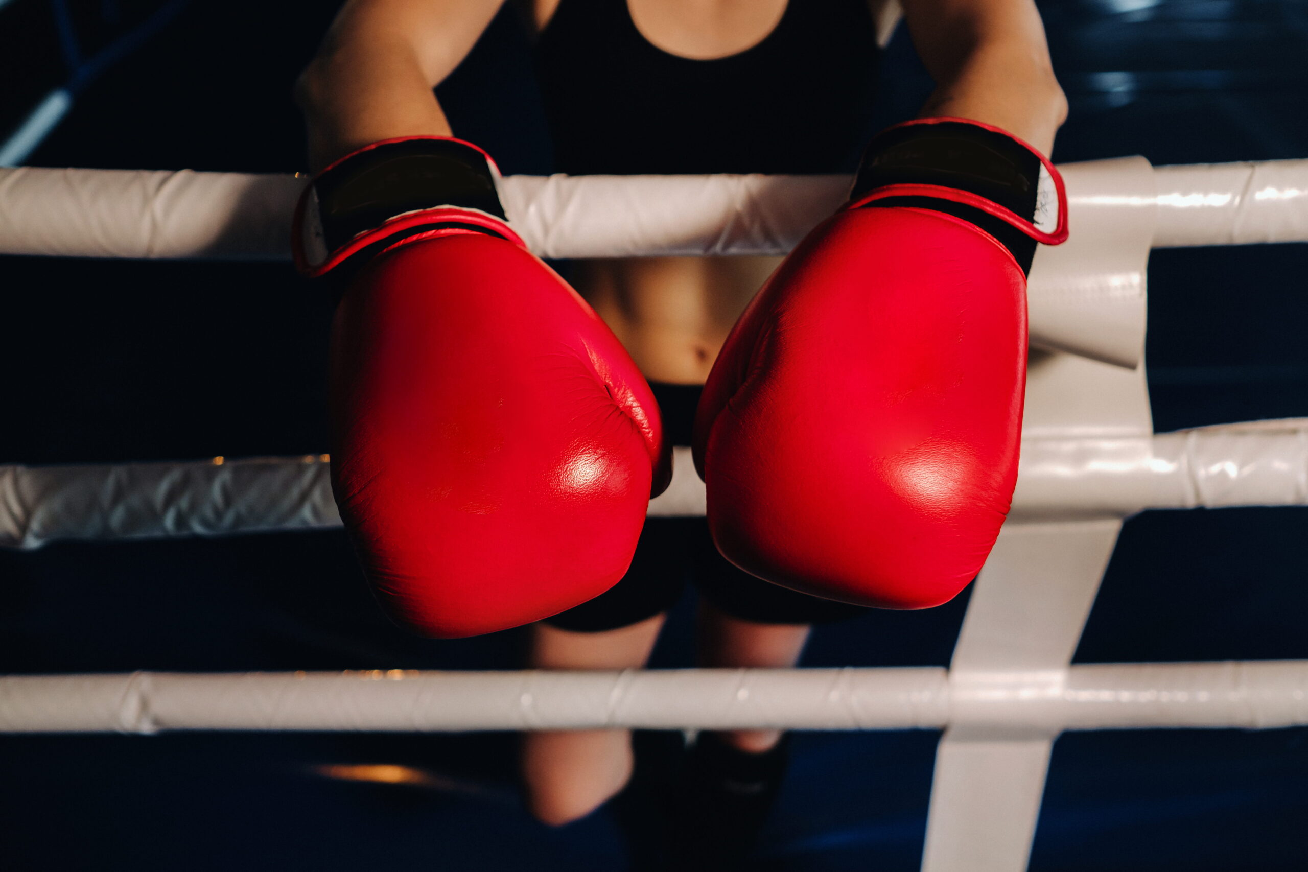 Boxer in red gloves leaning on the ropes of a boxing ring, ready for a match.