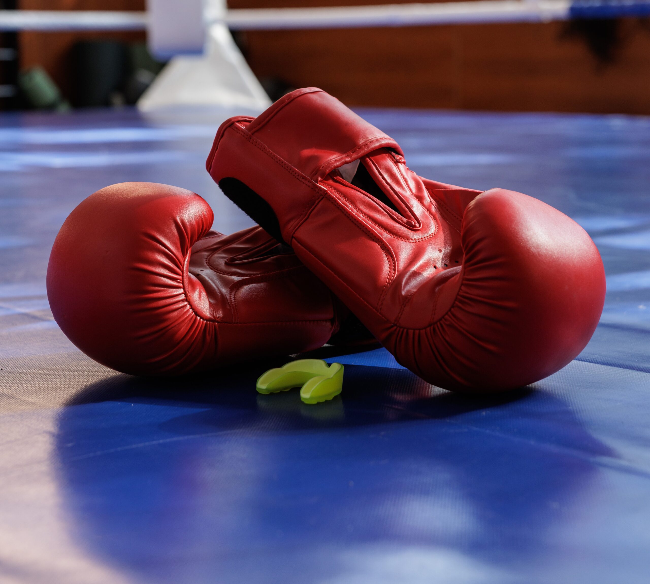 Red boxing gloves and mouthguard on a blue boxing ring mat.