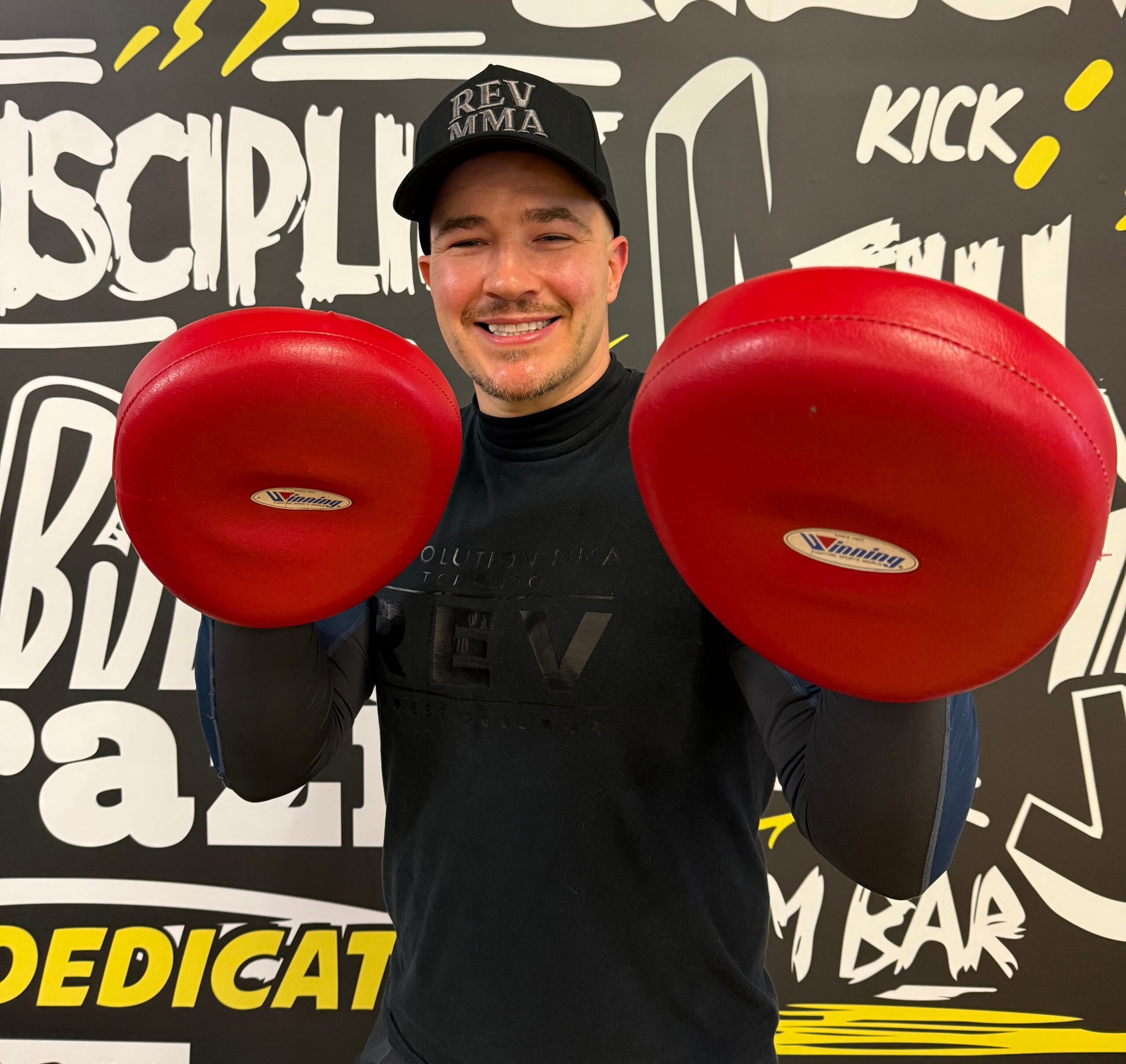 boxing-toronto-ontario-revmma Man holding red punching pads in a gym with motivational wall art.