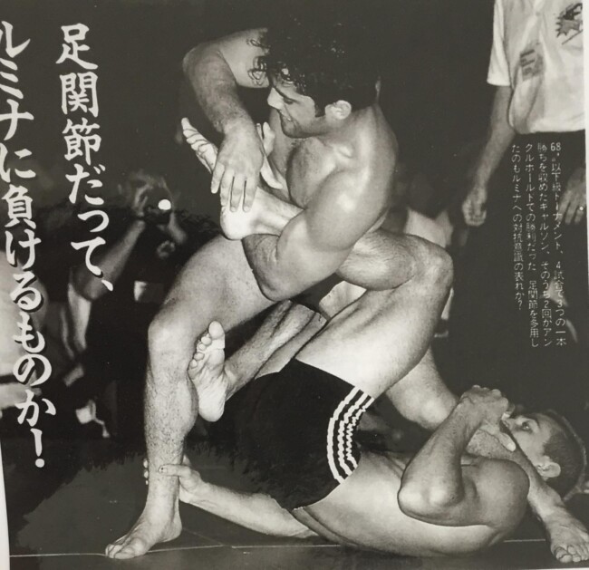 Joel winning by foot lock at the Canadian Jiu Jitsu Open. Photo by Japanese media Two athletes grappling in a martial arts match, one applying a leg lock technique.
