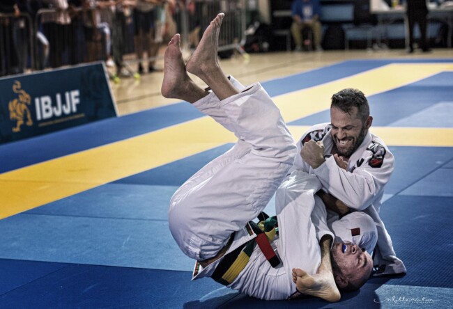Joel winning via arm bar submission, Toronto Open. Two Brazilian Jiu-Jitsu competitors grappling intensely at IBJJF tournament on blue mats.