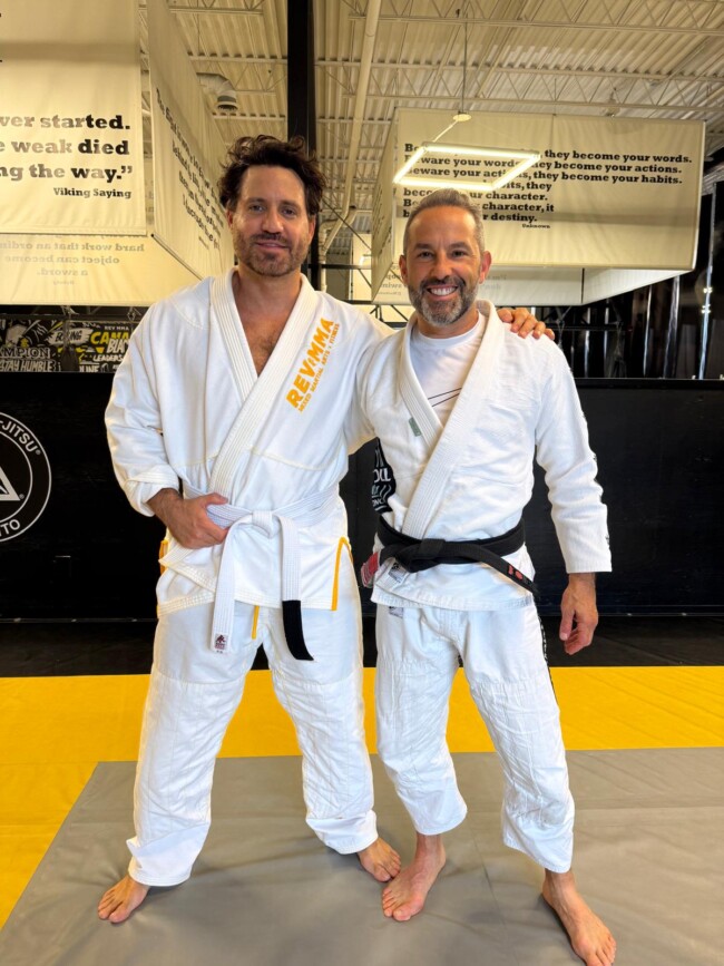 Joel training Hollywood actor Edgar Ramirez in Jiu Jitsu at RevMMA for his role in a Disney pilot. Two men in jiu-jitsu gis smiling at a martial arts gym with motivational quotes on walls.
