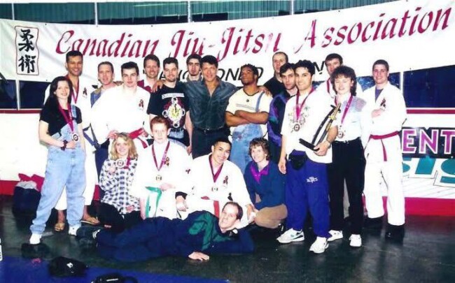 Joel after winning his division and the Open Weight division at the Canadian Open after defeating Carlos “The Ronin” Newton. Group of martial artists in front of Canadian Jiu-Jitsu Association banner, displaying medals and trophies.