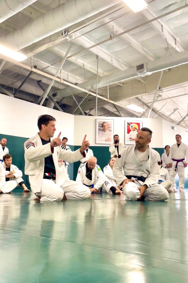 Joel assisting World Jiu Jitsu Champion and MMA legend Damian Maia at Gracie University, Los Angeles. Jiu-Jitsu class in session, instructor demonstrating techniques to students in a dojo.