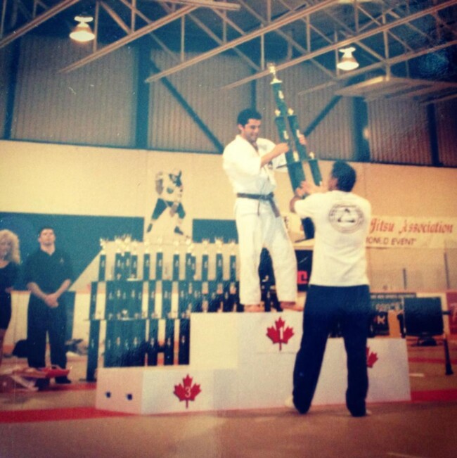 Joel receiving his trophy at the Canadian Open from jiu Jitsu legend Rickson Gracie. Martial artist celebrating victory, holding a large trophy on a podium in a Canadian Jiu-Jitsu event.
