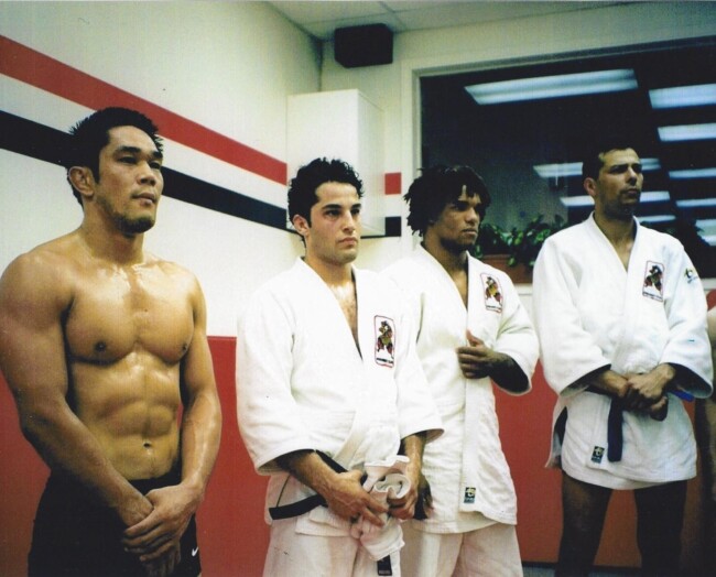 Joel Gerson, Rumina Sato, Carlos “The Ronin” Newton, at Samurai Club 1998. Group of four martial artists in a dojo, three wearing white gis, one shirtless, standing in a line.