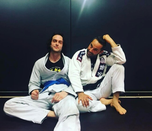 Joel training comedian Chris D’Elia at RevMMA in Toronto. Two men in Brazilian Jiu-Jitsu gis sitting on the mat, smiling and relaxed after training.
