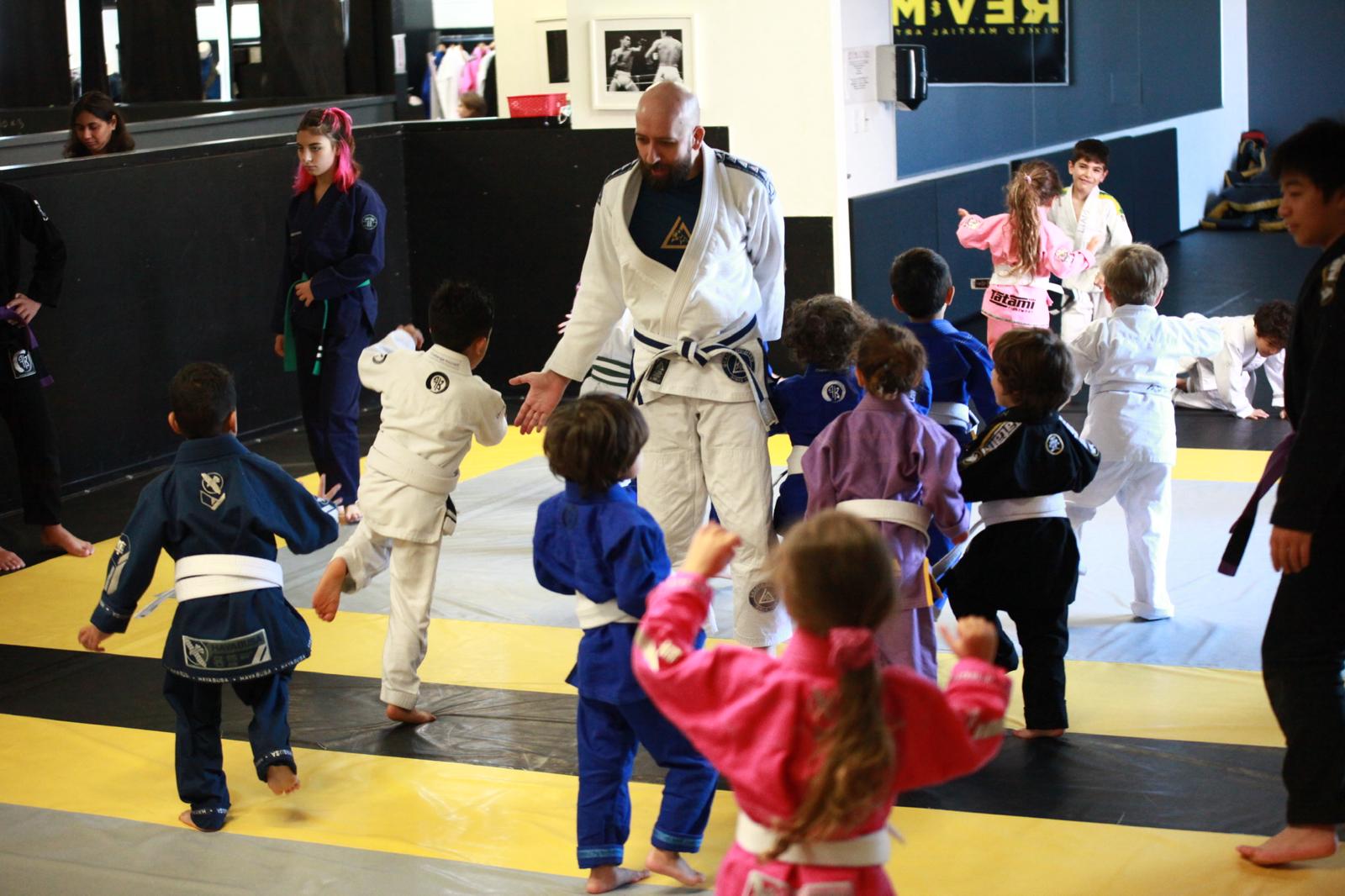 Kids practicing Brazilian Jiu-Jitsu in a dojo with instructor, wearing colorful gi uniforms, engaging in martial arts