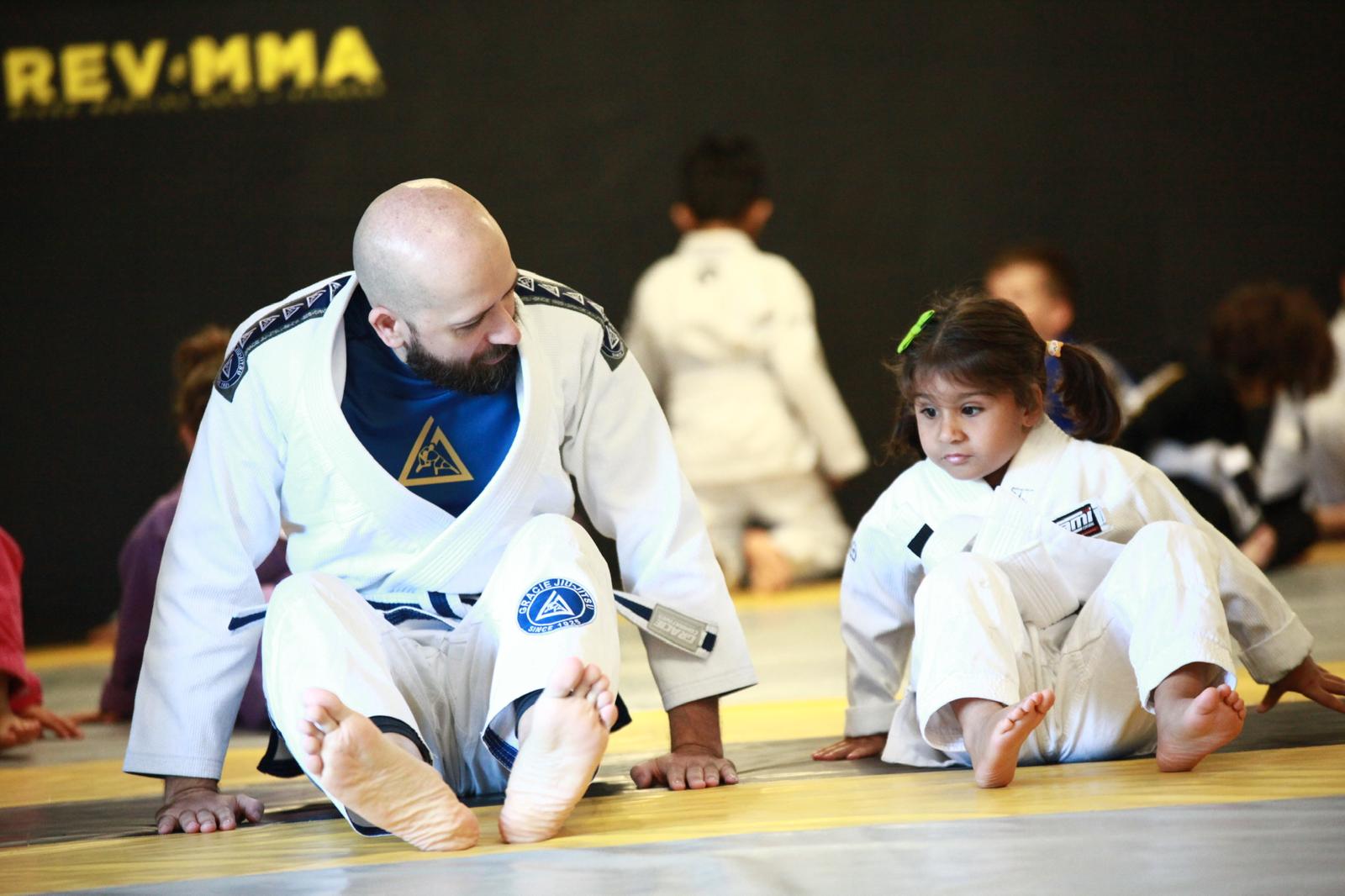Martial arts instructor teaching a young girl Brazilian Jiu-Jitsu on the mat, both in training attire.
