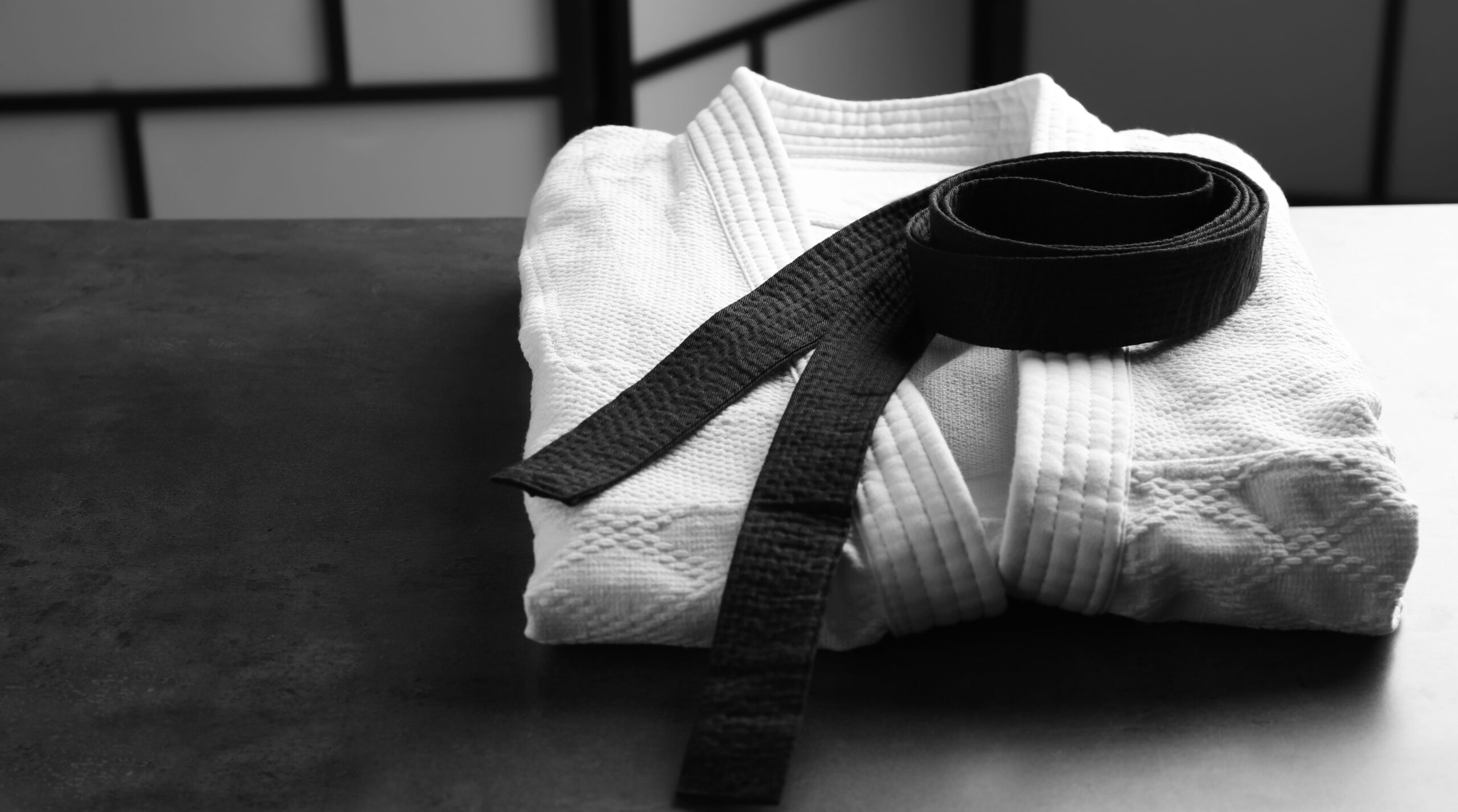 Folded martial arts gi with a black belt on dark surface, symbolizing discipline and achievement in BJJ.
