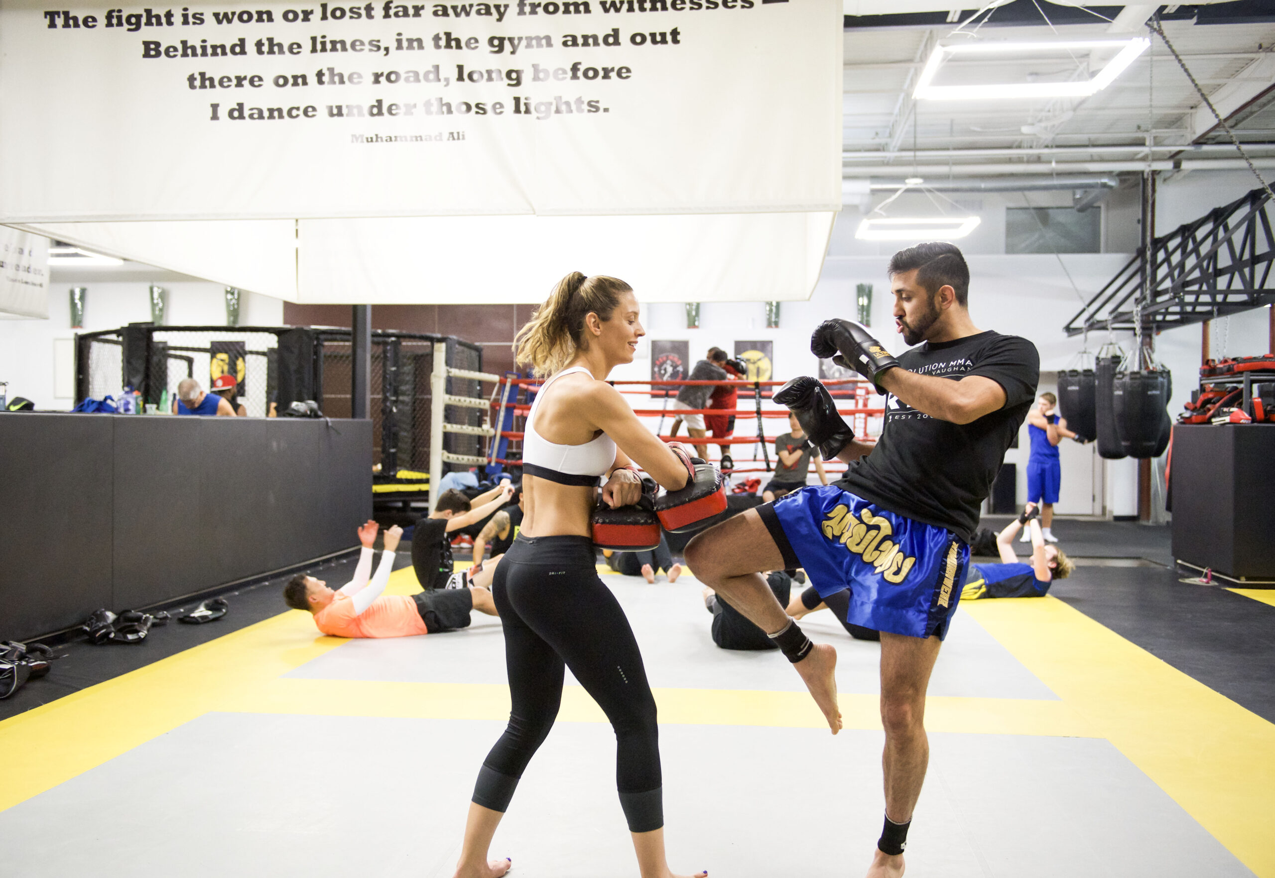 Coach holding pads while a member drives a high kick in a high-energy Toronto kickboxing session