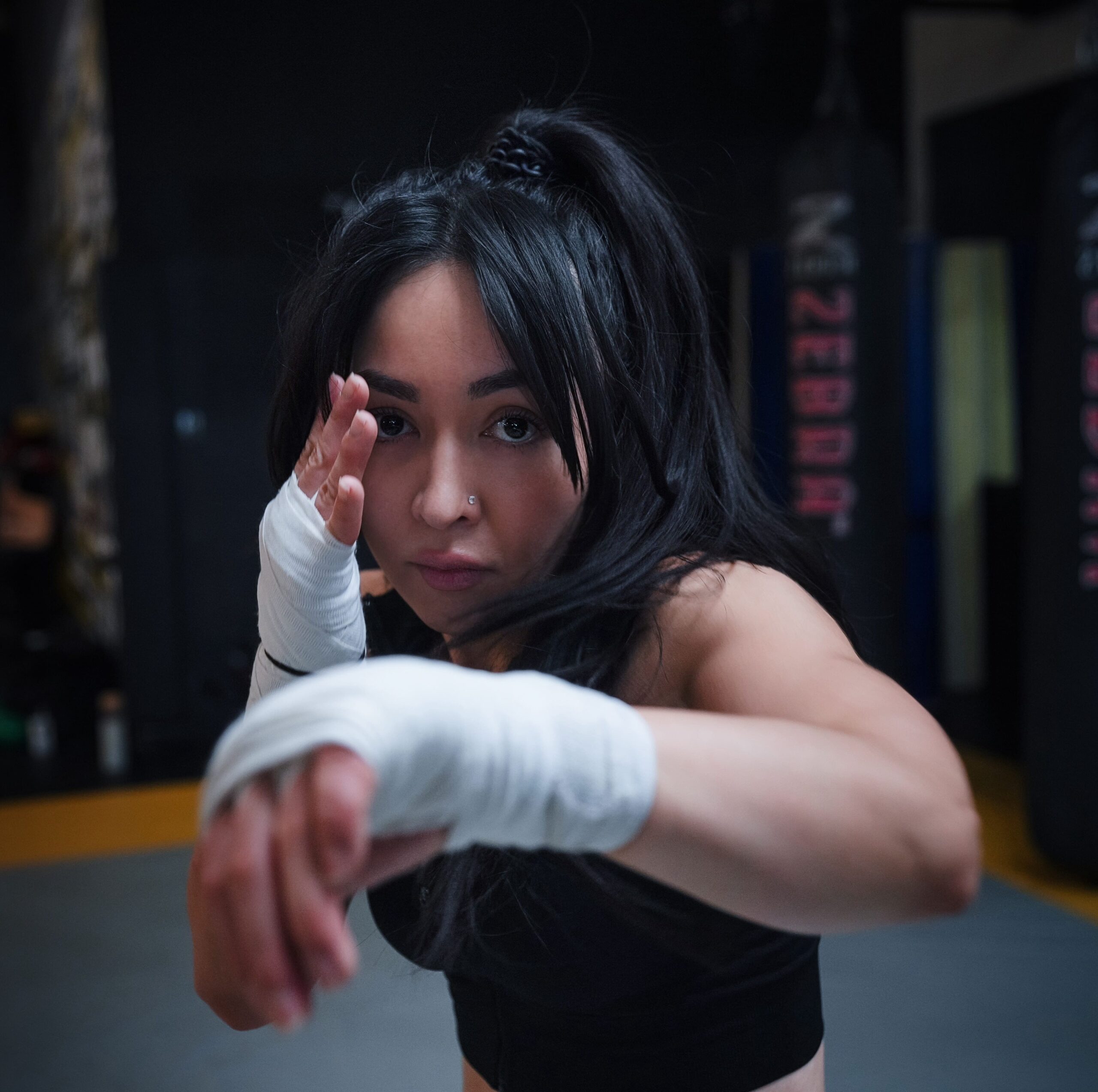 Woman practicing boxing with focus and hand wraps in a gym setting.