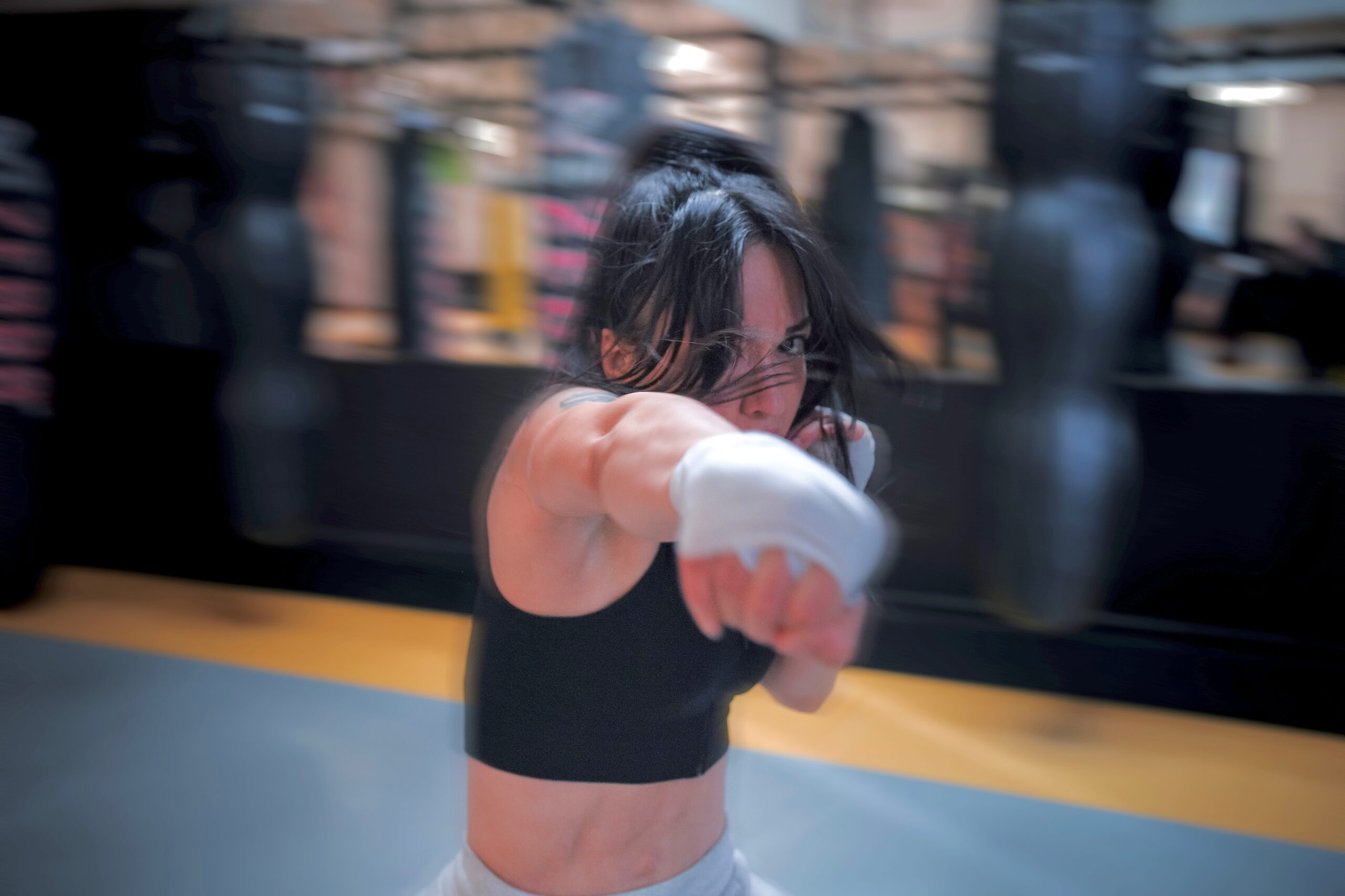 Woman boxing in gym, focused on punching with wrapped hands. Fitness and martial arts training.